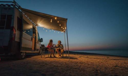 Young Caucasian heterosexual couple near the camper van parked near  the sea at sunset